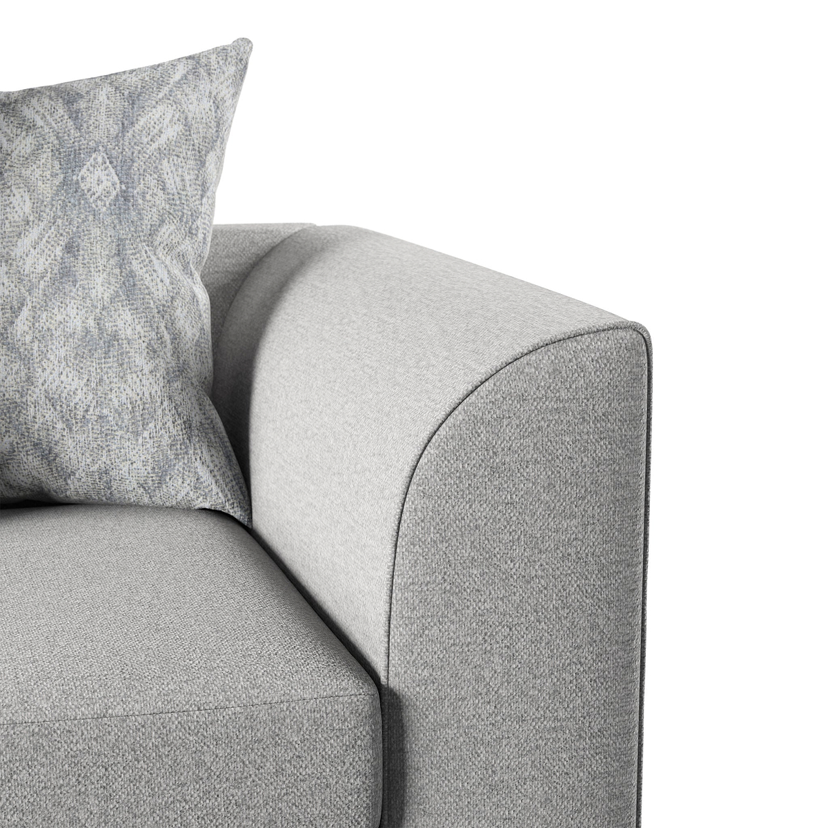 A patterned pillow rests against the curved, grey upholstered arm of a sofa, depicting a close-up of comfortable home furniture.