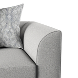 A patterned pillow rests against the curved, grey upholstered arm of a sofa, depicting a close-up of comfortable home furniture.
