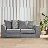 A grey sofa with cushions sits idle in a room with a vertical slat wall, a potted plant, and soft lighting.