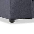 A close-up of a grey upholstered sofa corner, focusing on its textured fabric and a black plastic leg against a white background.