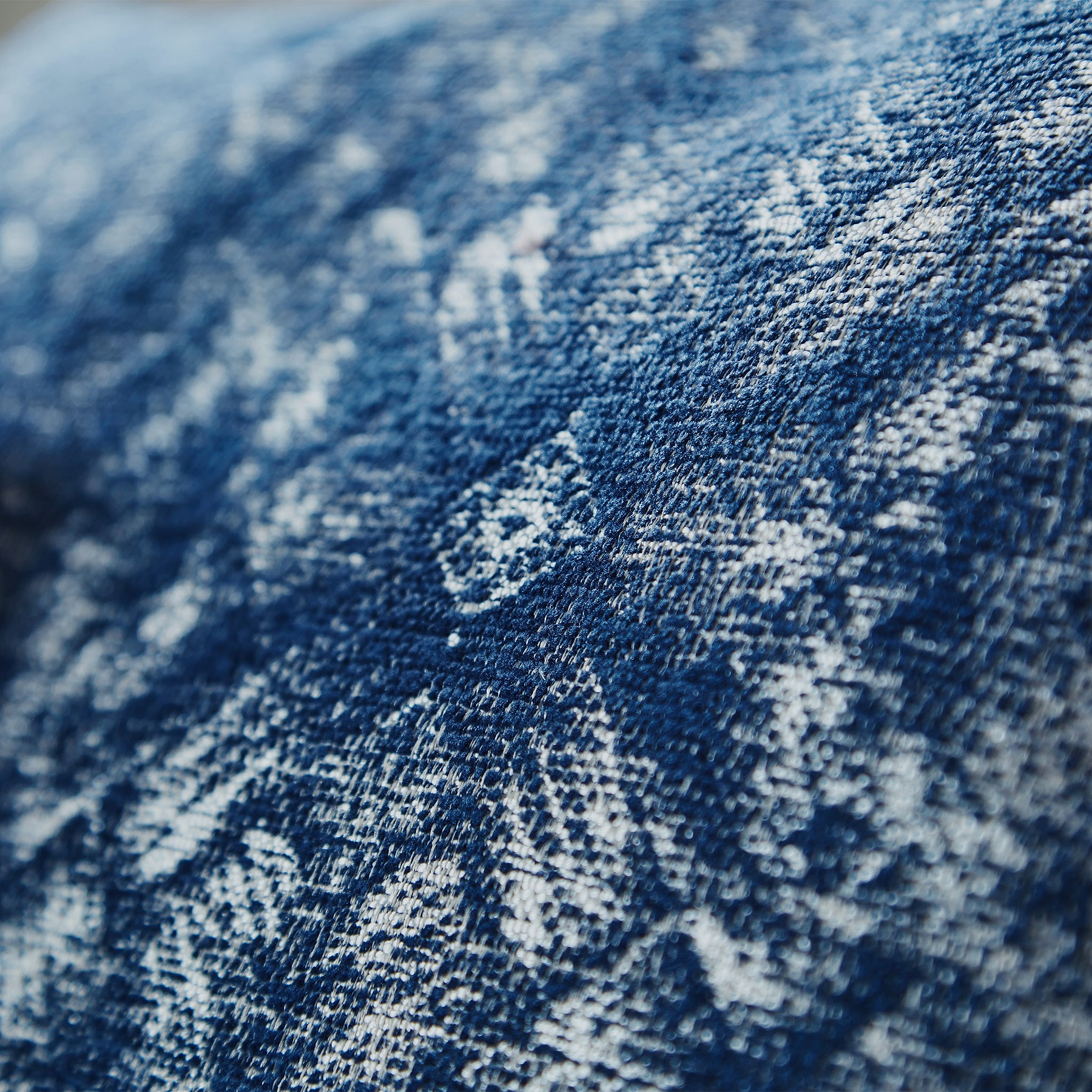 Close-up texture of denim fabric showing intricate white threading against the predominant blue, highlighting the classic weave pattern of jeans.