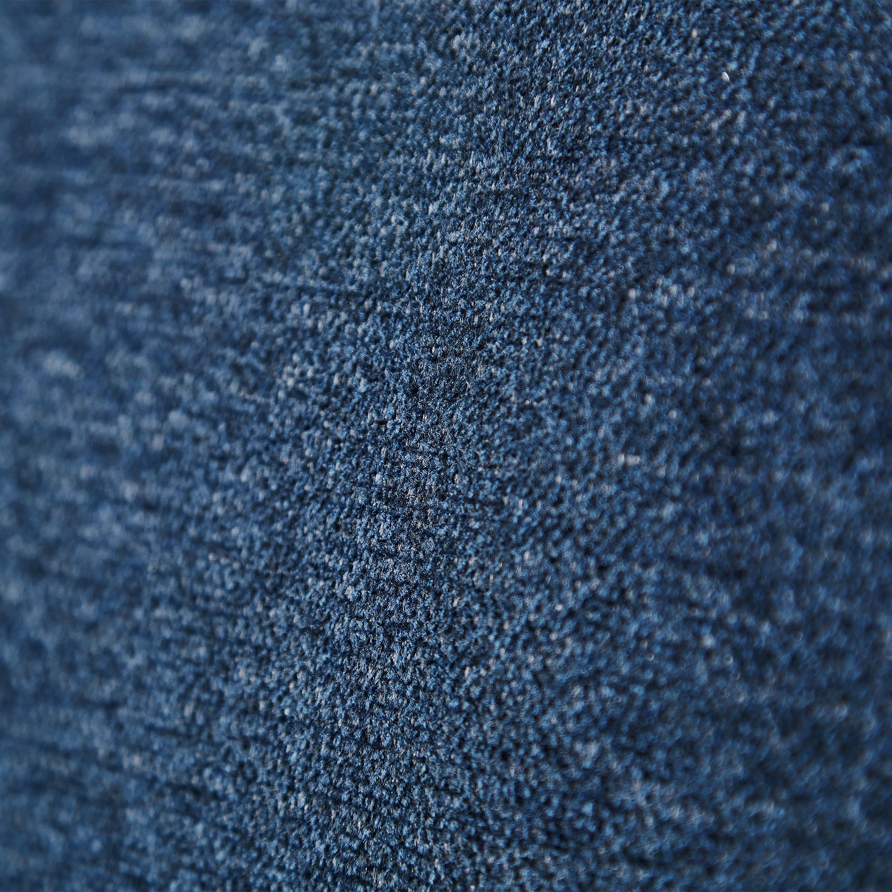 A close-up of a textured blue denim fabric, showing intricate weaves and fibers with a soft, fuzzy appearance.