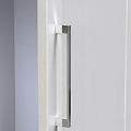 A silver, vertical door handle on a white textured door, partially opened against a light grey wall, indoor setting, with light shadowing.