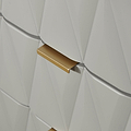 A golden handle protrudes from a textured white surface with geometric patterns, possibly a modern door or cabinet.