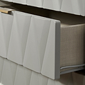 A white, textured radiator cover with a geometric pattern is attached to a wall above a grey heating unit, set against a contrasting beige wall.