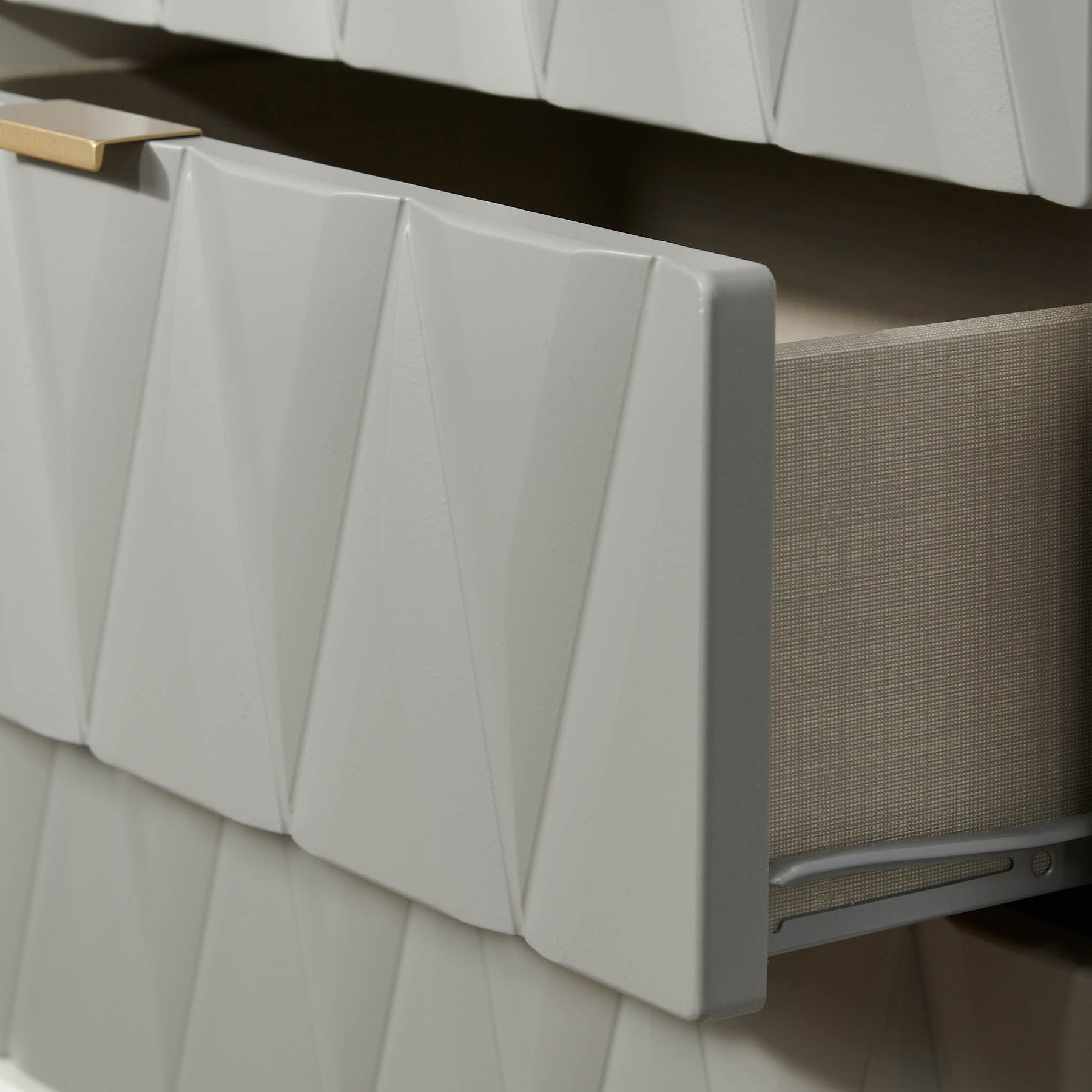 A white, textured radiator cover with a geometric pattern is attached to a wall above a grey heating unit, set against a contrasting beige wall.