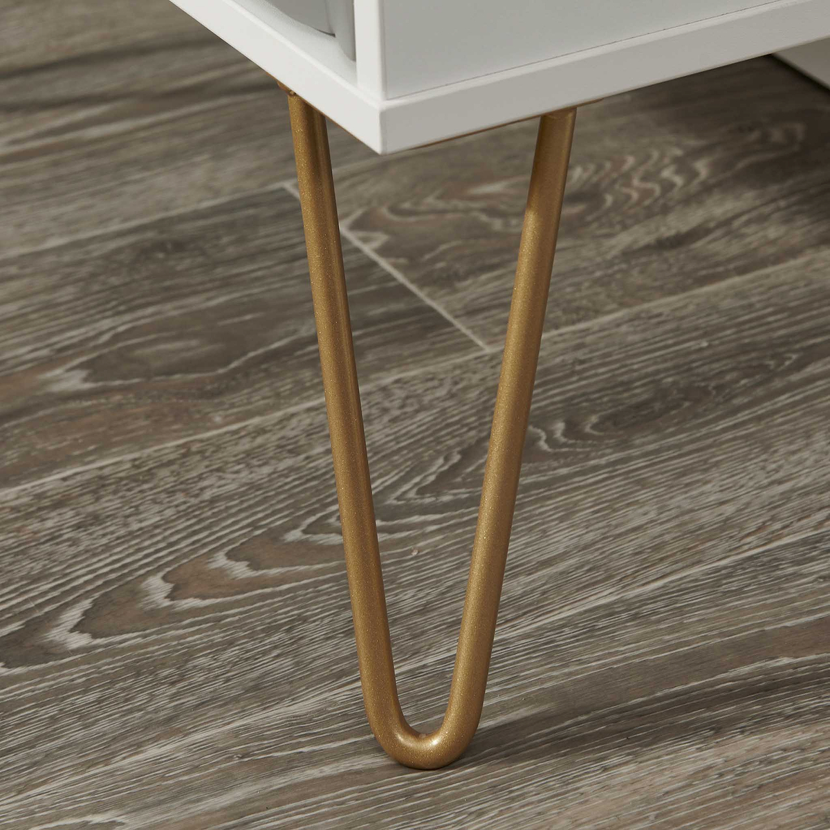 Gold-colored table leg stands on a textured wooden floor, part of a white table structure visible at the top.