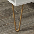 Slim, golden-colored metal legs support a white structure on a textured wooden floor, likely a piece of furniture in an indoor setting.