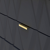 A gold-colored, horizontal mail slot is set into a dark, textured wall with geometric angular patterns.