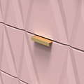 Golden rectangular drawer handle on a pink faceted wall, light subtly accentuating its color and shape.