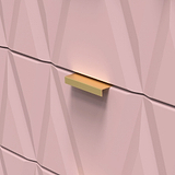 Golden rectangular drawer handle on a pink faceted wall, light subtly accentuating its color and shape.