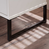 A white rectangular cabinet rests on black metal legs, casting soft shadows on a wooden floor with a striped light pattern from a window.