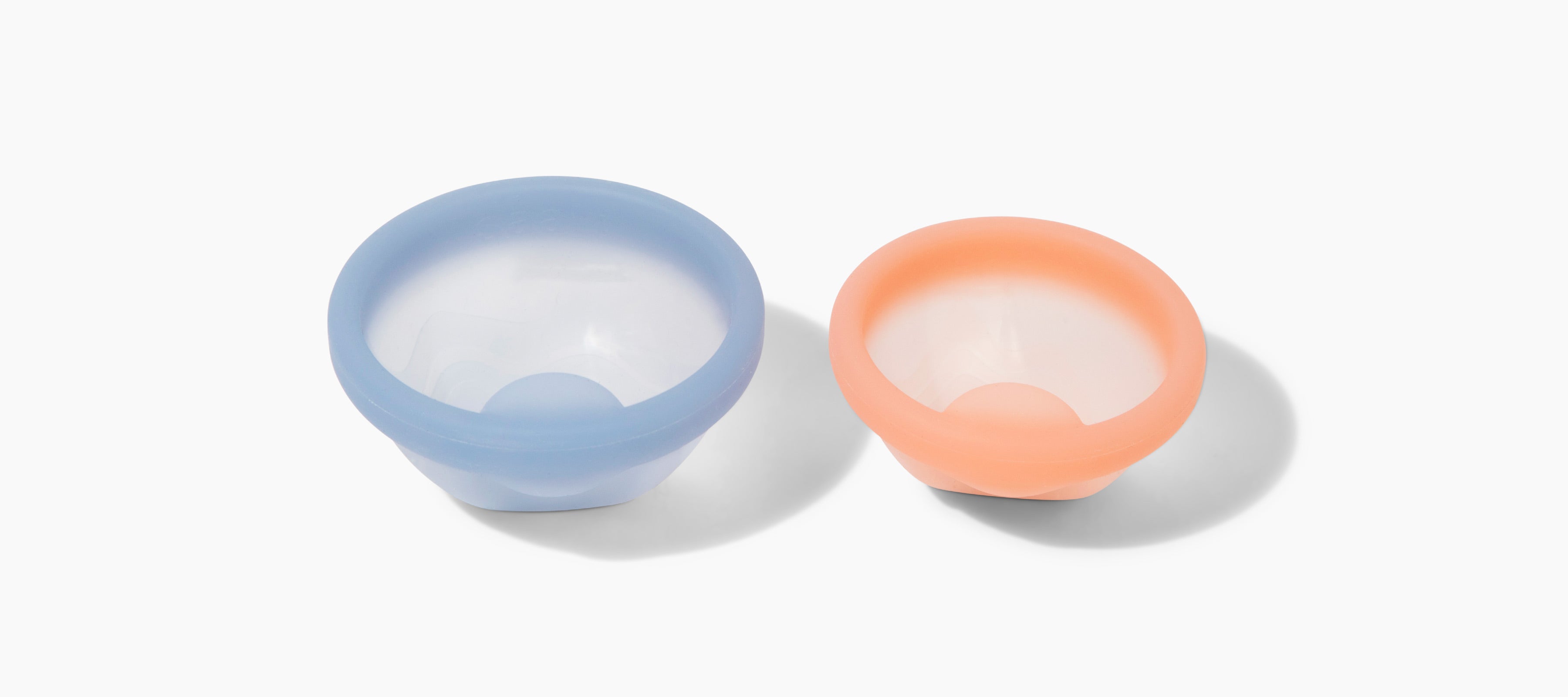 Two reusable silicone menstrual cups in light blue and peach displayed on a white background.