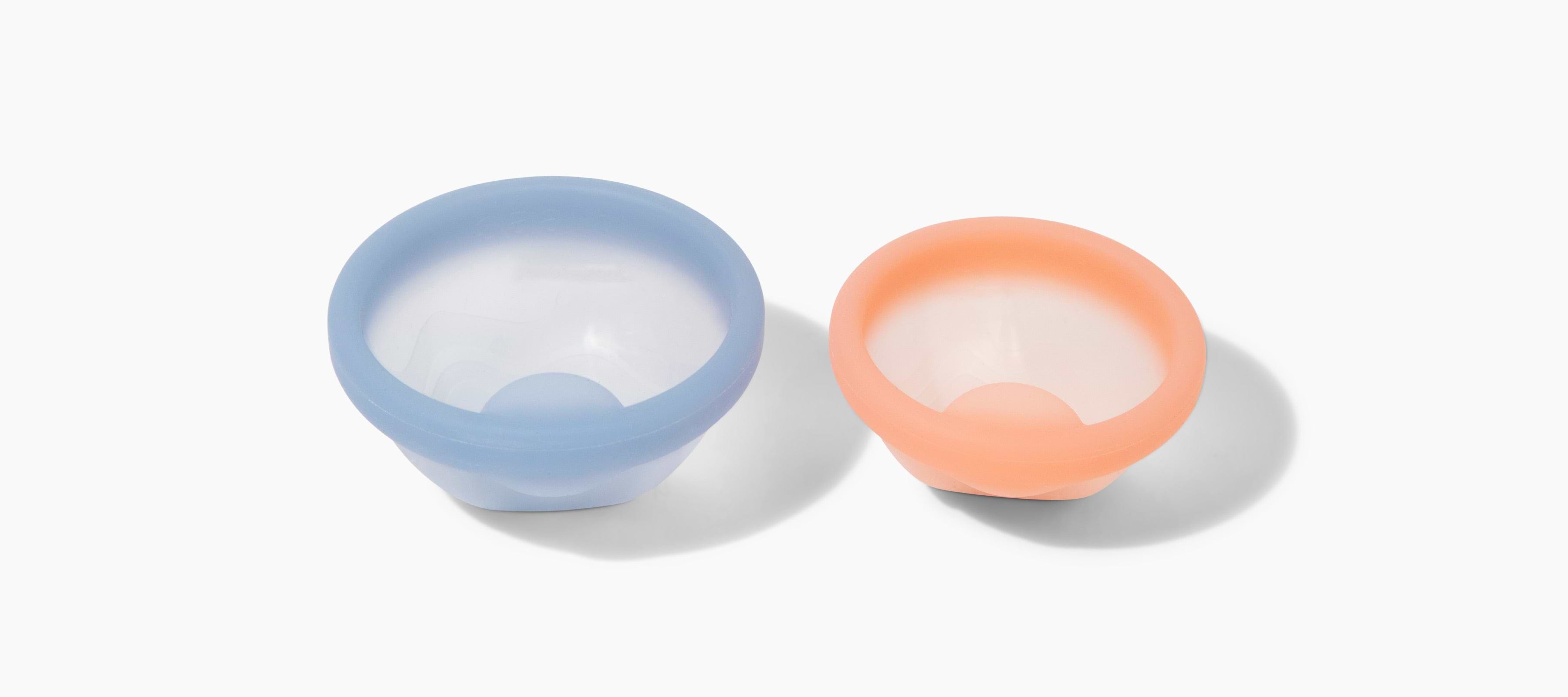 Two reusable silicone menstrual cups in light blue and peach displayed on a white background.