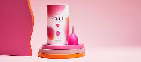 Saalt menstrual disc packaging and pink menstrual cup displayed on layered pink and orange podiums