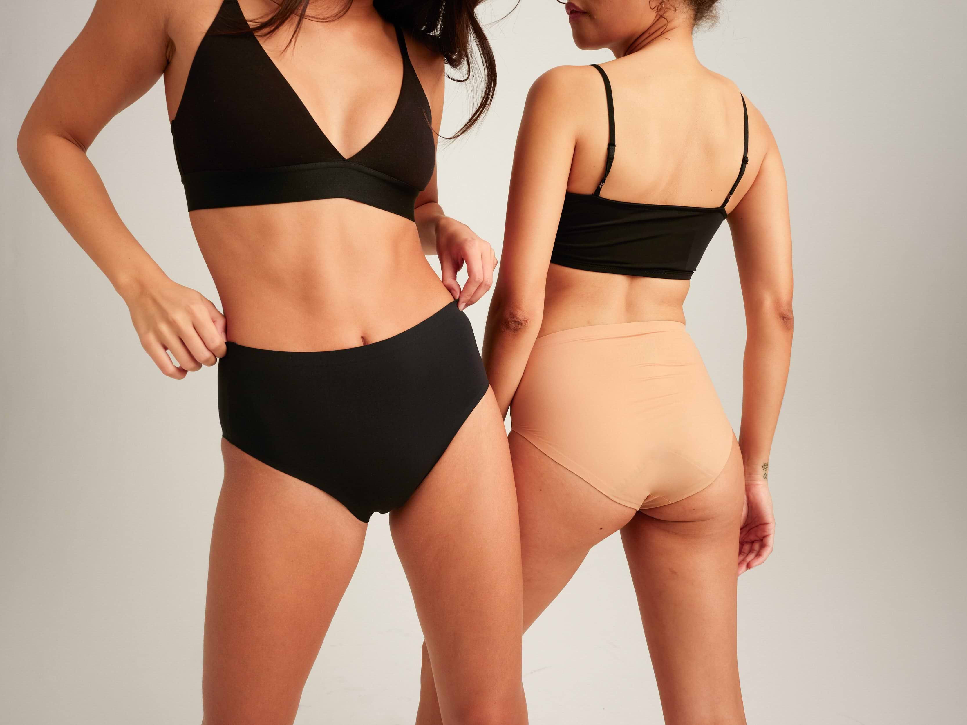 Two models in black bras and high-waisted period underwear, front and back views on neutral background.