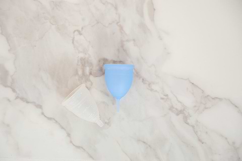 Two reusable menstrual cups, one blue and one translucent white, placed on a light marble surface.