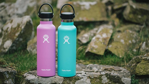 Purple and turquoise Hydro Flask water bottles standing on rocks outdoors.