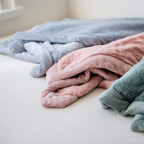 Soft pastel blankets folded on a bed near a window.