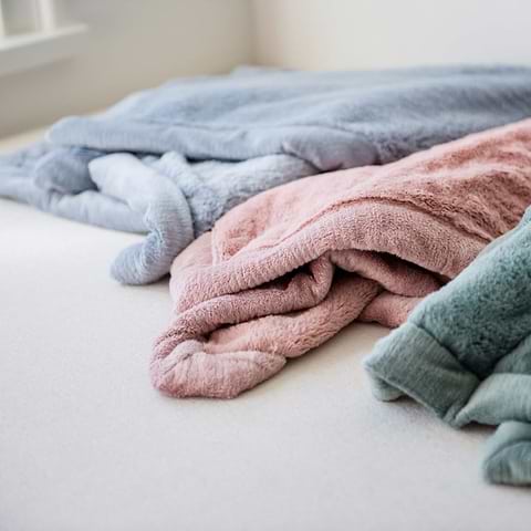 Soft pastel blankets folded on a bed near a window.