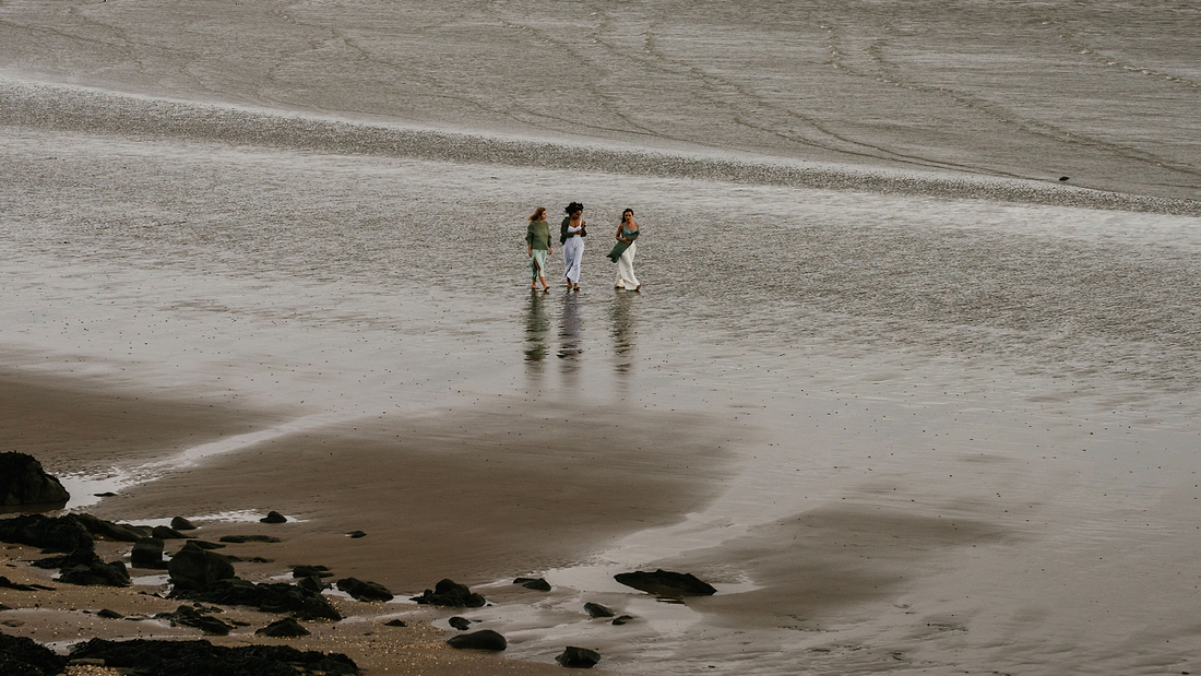 Three people walking together across wet sand on a quiet beach.