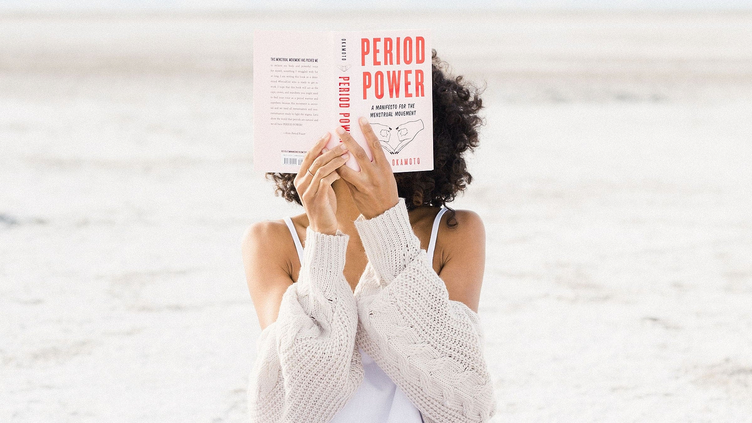 Person holding the book “Period Power” while sitting outdoors in a cozy sweater.