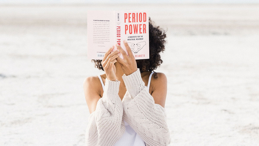 Person holding the book “Period Power” while sitting outdoors in a cozy sweater.