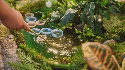 Pastel menstrual cups float in a lush pond scene, blending sustainability, nature, and mindful self-care.