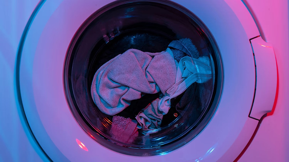 Reusable underwear and towels inside a washing machine drum lit with blue and pink lighting.