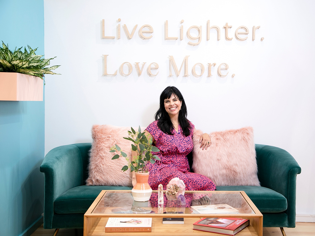 Woman sitting on a green couch beneath a “Live Lighter. Love More.” wall sign.