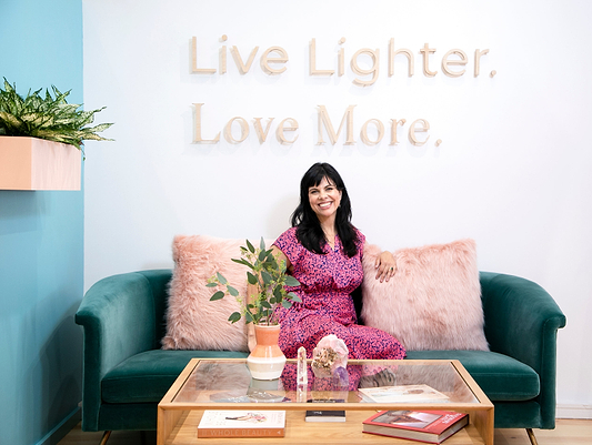 Woman sitting on a green couch beneath a “Live Lighter. Love More.” wall sign.
