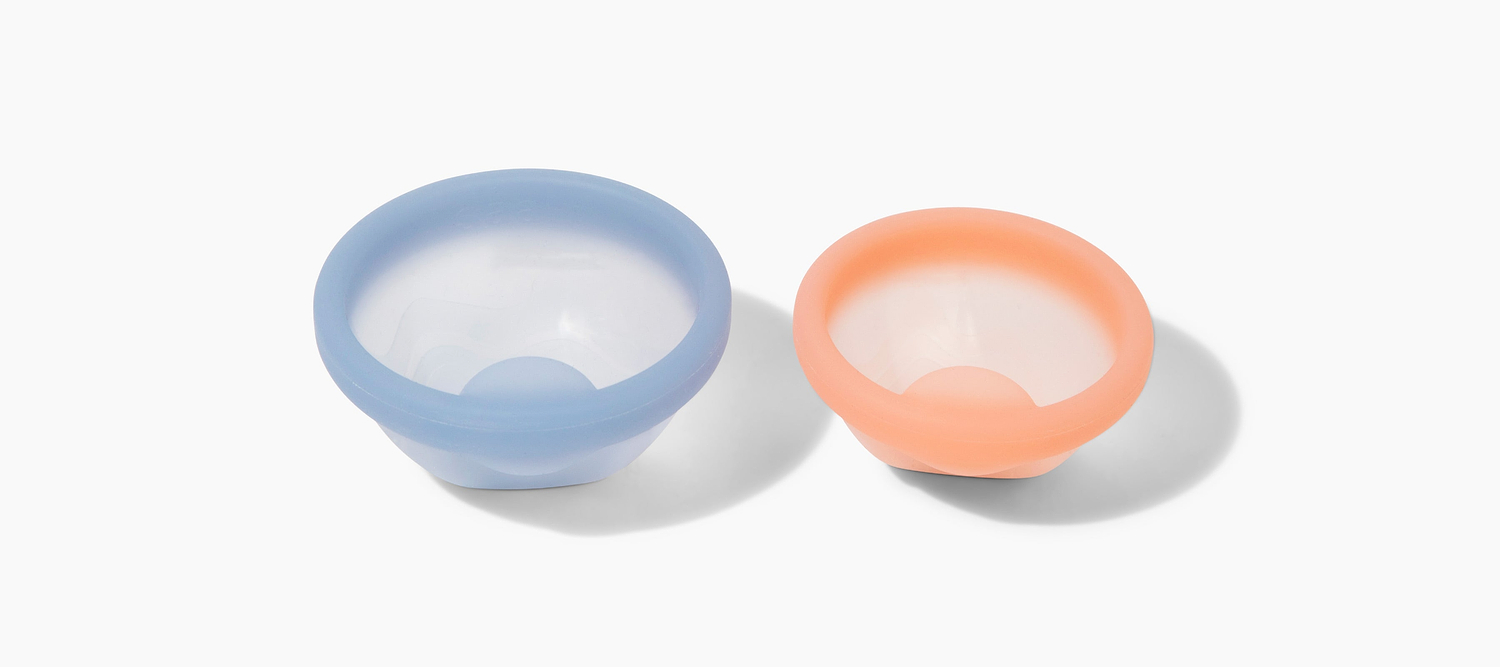 Two reusable silicone menstrual discs in blue and peach displayed on a light gray background