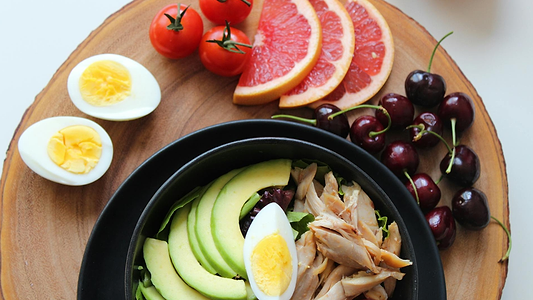 Healthy meal bowl with avocado, egg, and chicken, served with grapefruit, cherries, tomatoes, and eggs.