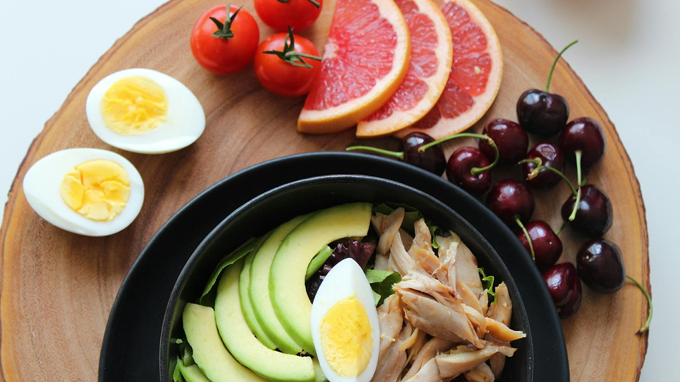 Healthy meal bowl with avocado, egg, and chicken, served with grapefruit, cherries, tomatoes, and eggs.