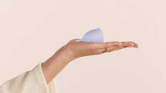 Hand holding a light blue menstrual cup against a soft neutral background