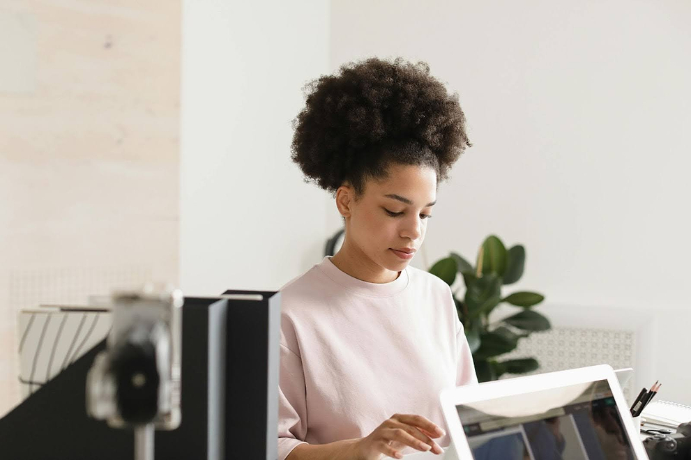 Woman with natural curly hair working at a desk with a laptop in a bright modern office.