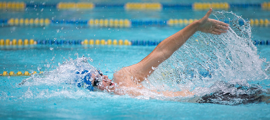 Swimmer in a pool performing freestyle stroke, arm extended forward with water splashing around.