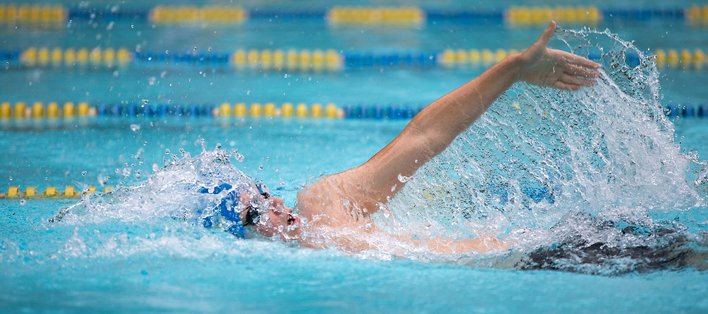Swimmer in a pool performing freestyle stroke, arm extended forward with water splashing around.