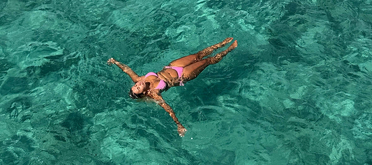 Women in a pink swimsuit floating on their back in clear turquoise water.