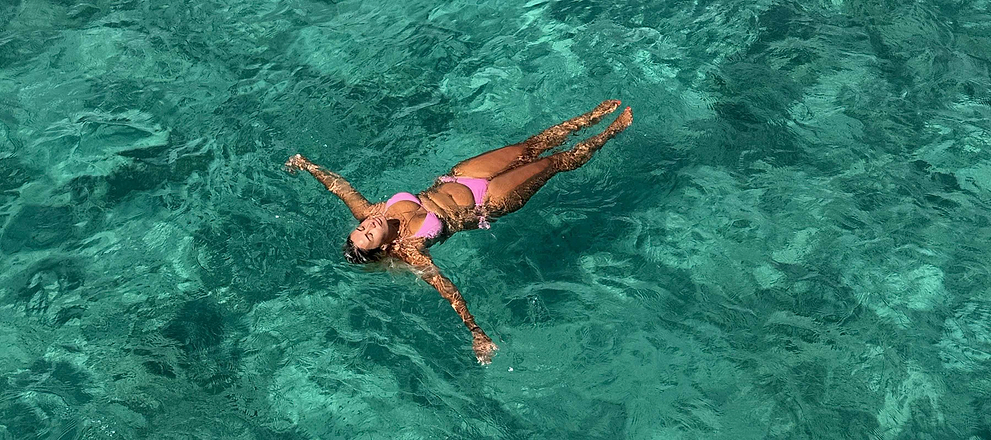 Women in a pink swimsuit floating on their back in clear turquoise water.