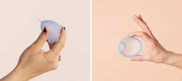 Hands holding a light blue menstrual cup from side and top views against a soft pastel background.