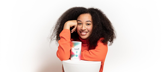 Smiling person in an orange sweater posing with Saalt menstrual disc packaging against a white background