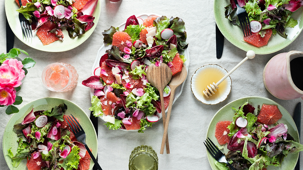 Colorful fresh salad spread with grapefruit, greens, and radishes served on multiple plates.