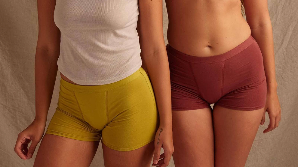 Two people modeling colorful fitted boxer-style underwear against a neutral indoor backdrop.