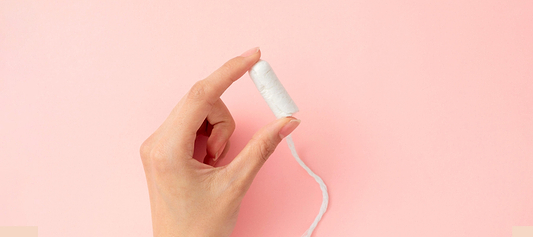 Hand holding a white tampon against a pink background.