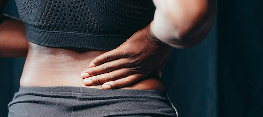 Person in athletic wear holding lower back, suggesting back pain or muscle strain.