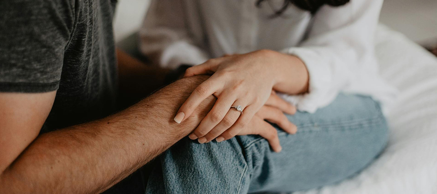 Close-up of a person holding another’s hand, showing an engagement ring.