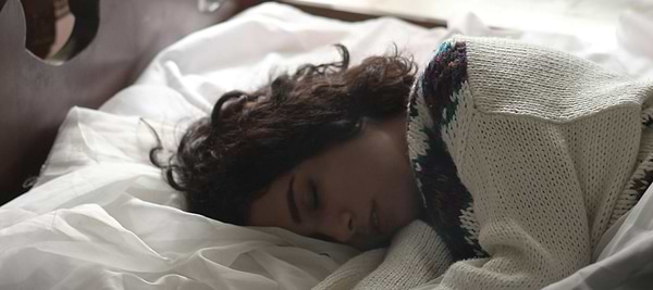 Person sleeping peacefully in bed under a cozy knit sweater, illustrating why is it ok to sleep more during period fatigue.