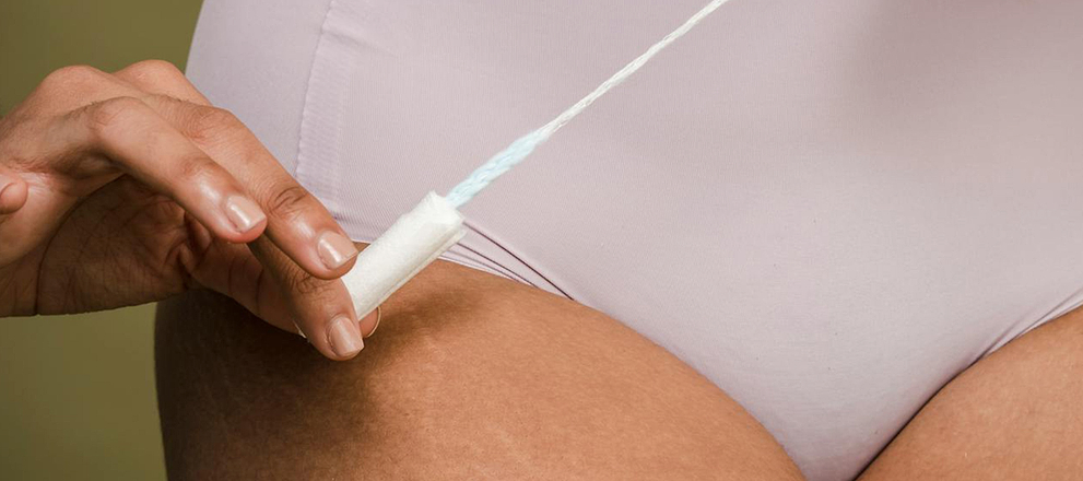 A person pulls a tampon string while wearing light-colored underwear in a close-up view.