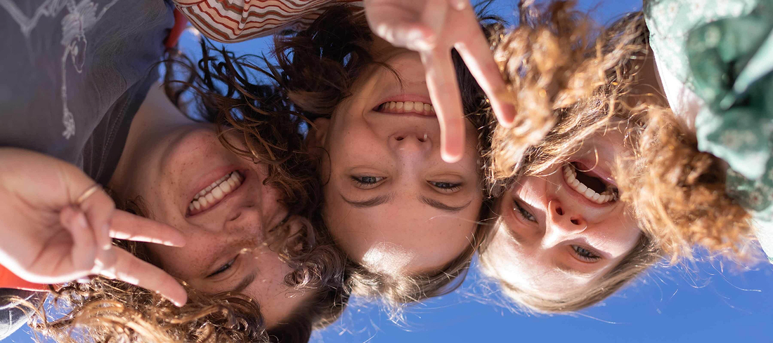 Three smiling friends posing together outdoors under a bright blue sky.